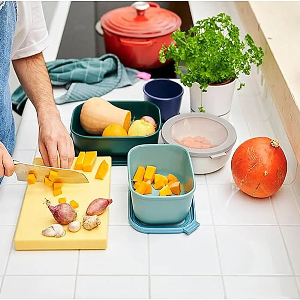 Person preparing vegetables on a cutting board with containers holding chopped vegetables in a kitchen.