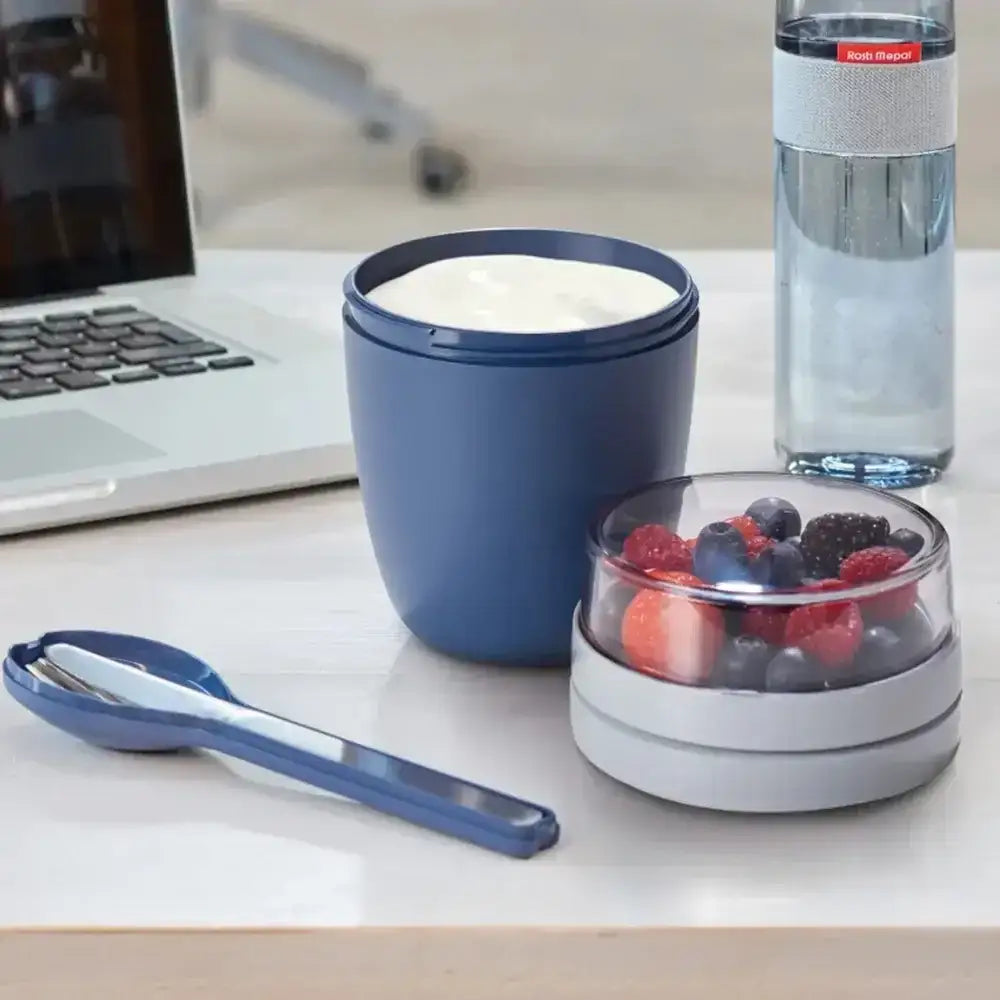 Blue snack container with yogurt and berries on a desk next to a laptop and water bottle.