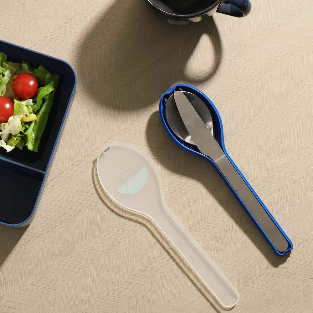 Spoon and knife set with blue handle on a beige surface next to a salad container.