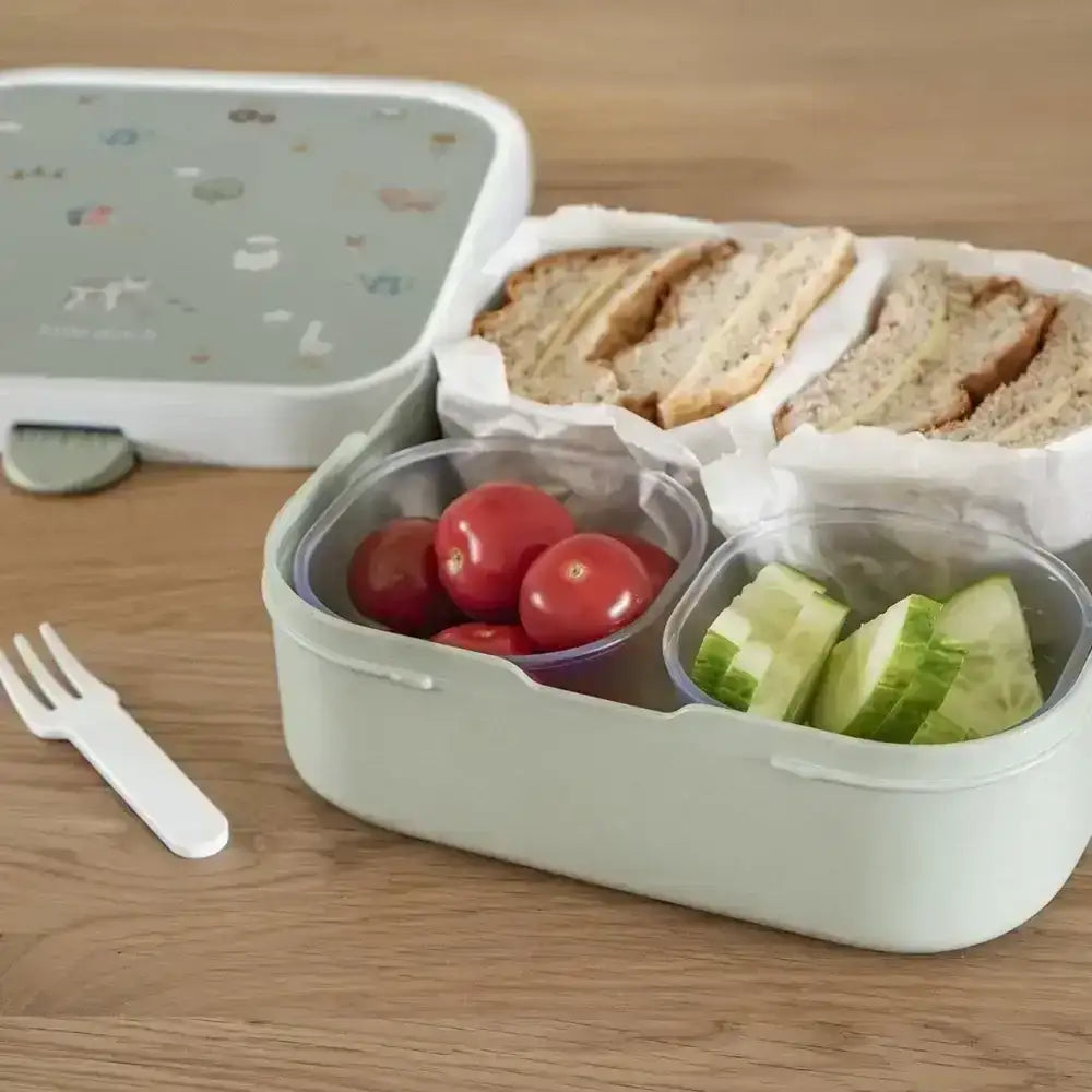 Bento box with compartments containing bread, tomatoes, and cucumbers on a wooden surface.