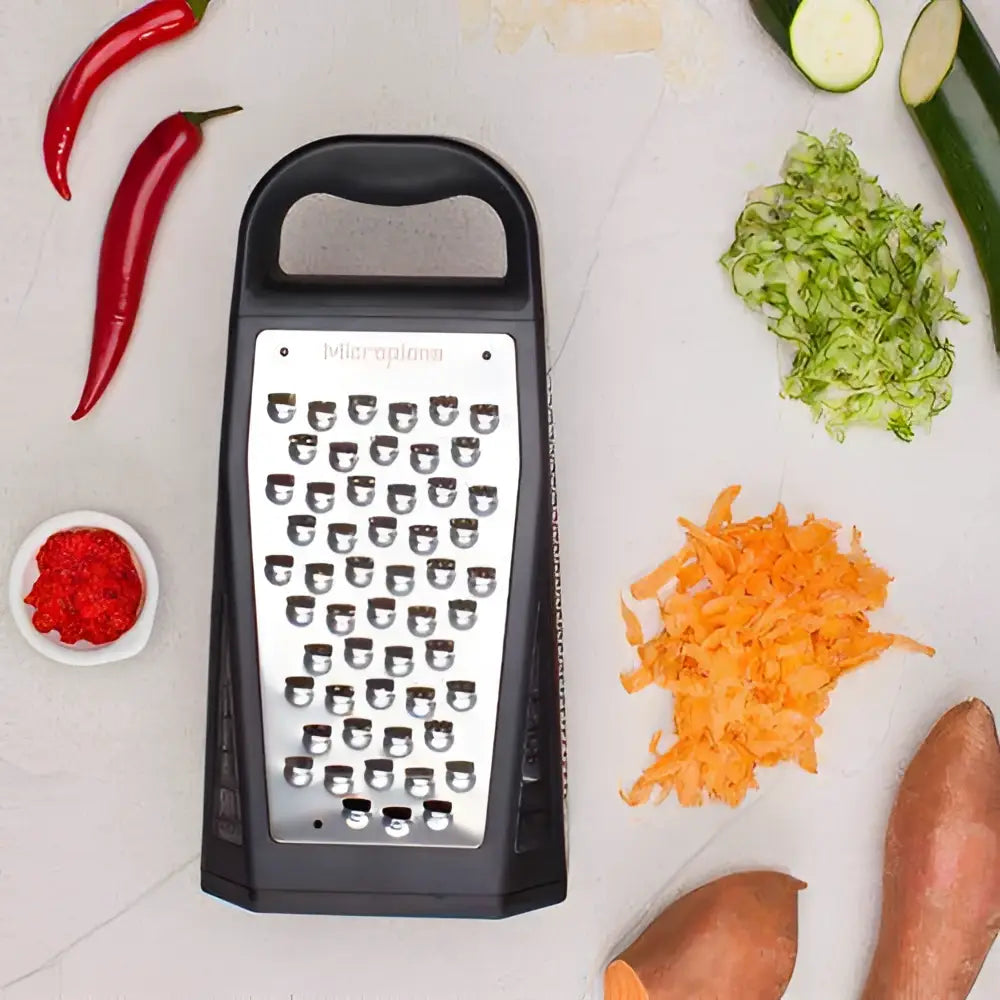 Black box grater with shredded vegetables on a light surface