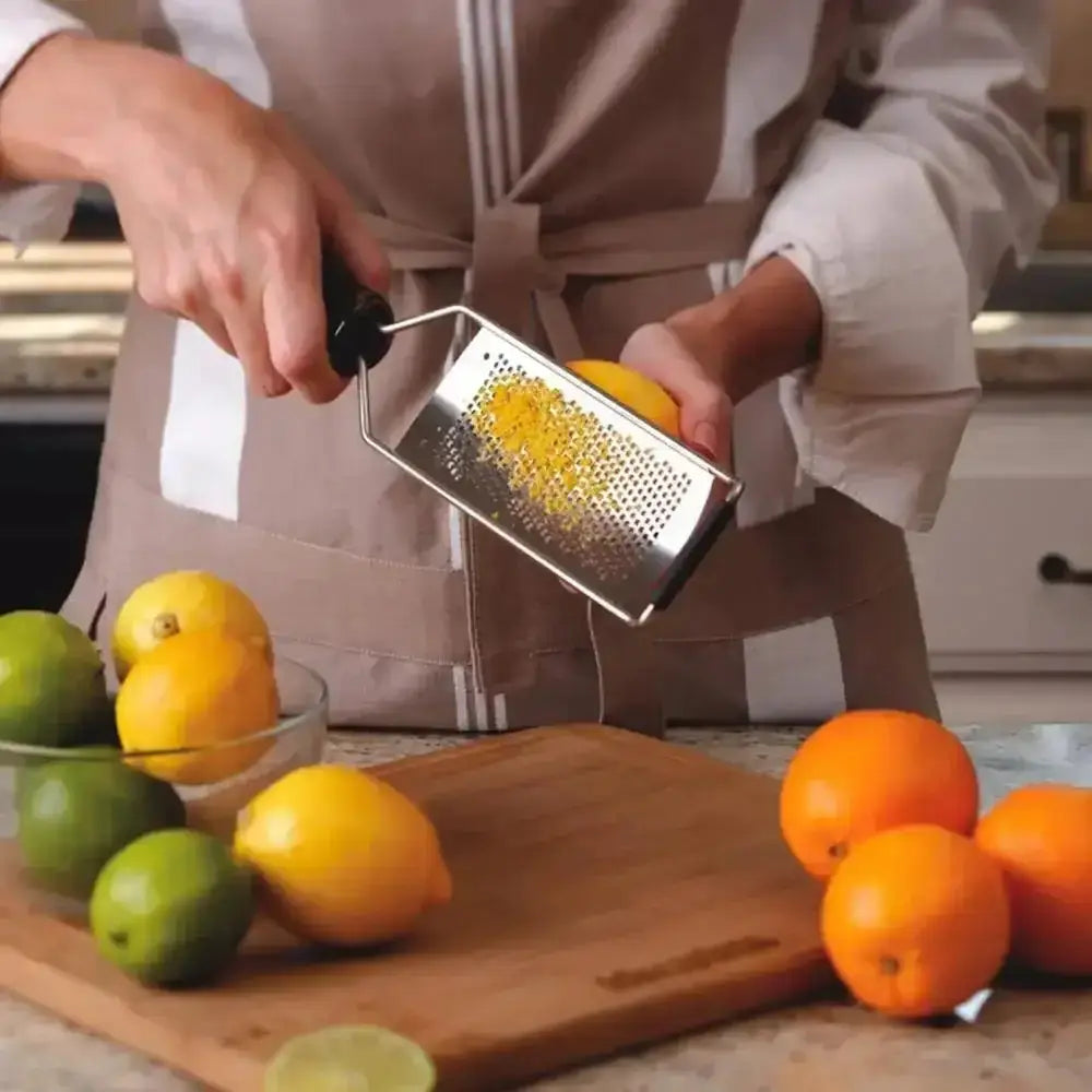Person grating lemon on a wooden cutting board with fruits around