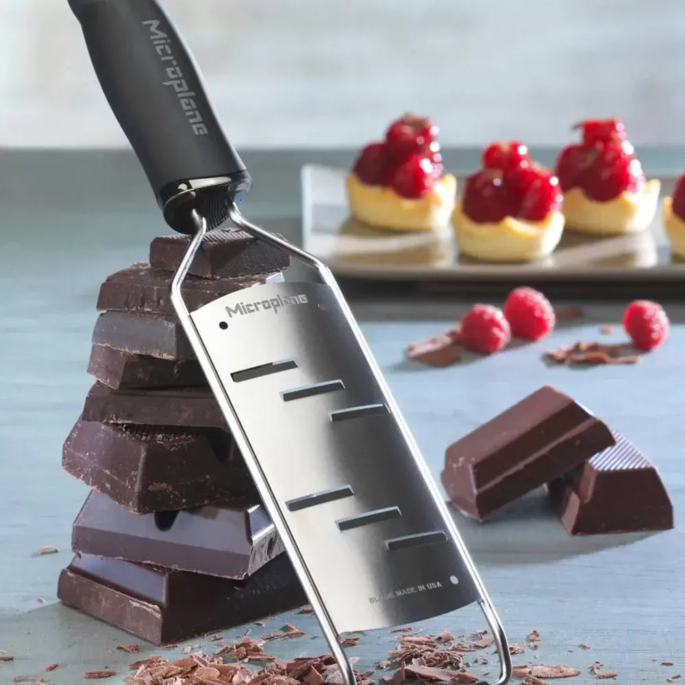 Micropplane chocolate shaver with stacked chocolate bars and a blurred dessert background