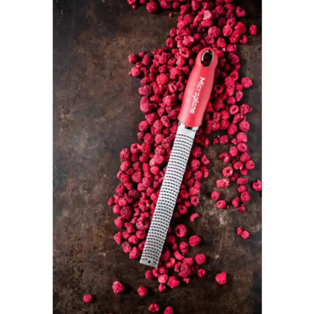 Red microplane grater on raspberries with a dark background