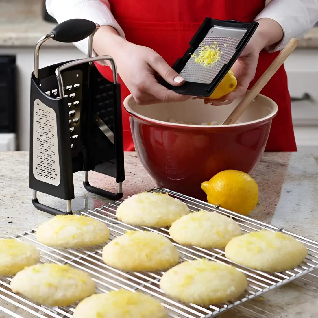 Person grating lemon zest into a bowl with cookies on a cooling rack.