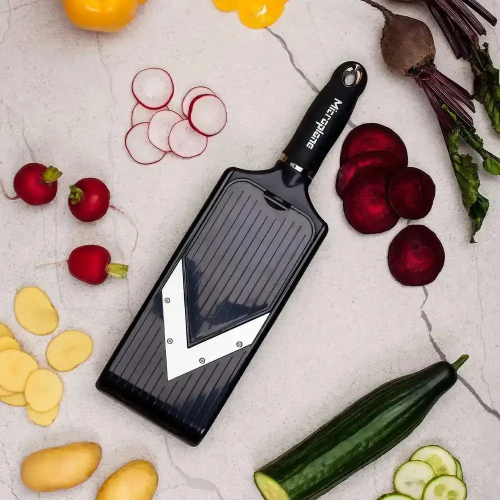 Microplane grater with brand name surrounded by sliced vegetables on a light surface