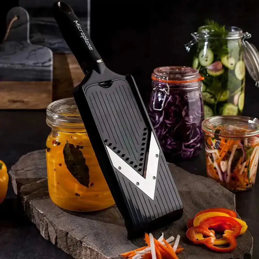 Microplane grater on a wooden board with jars of pickled vegetables in the background