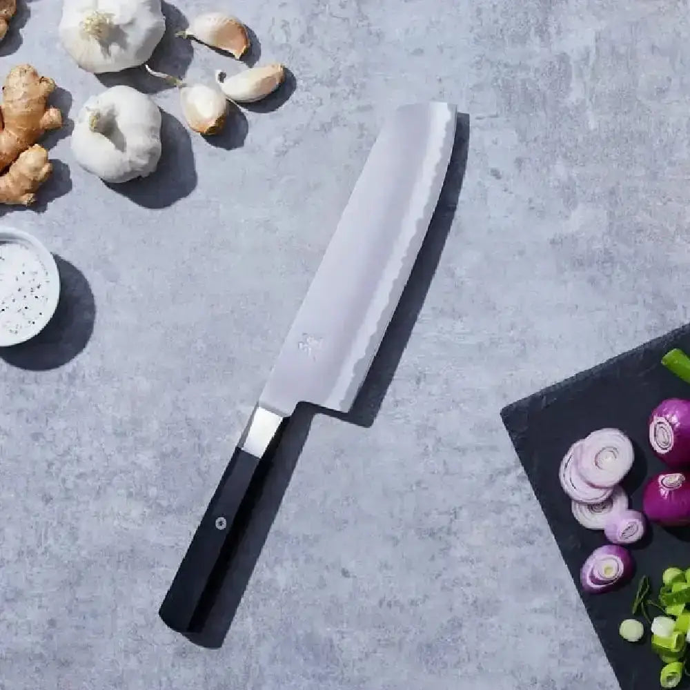 Knife on a gray surface with garlic, ginger, and onions around it