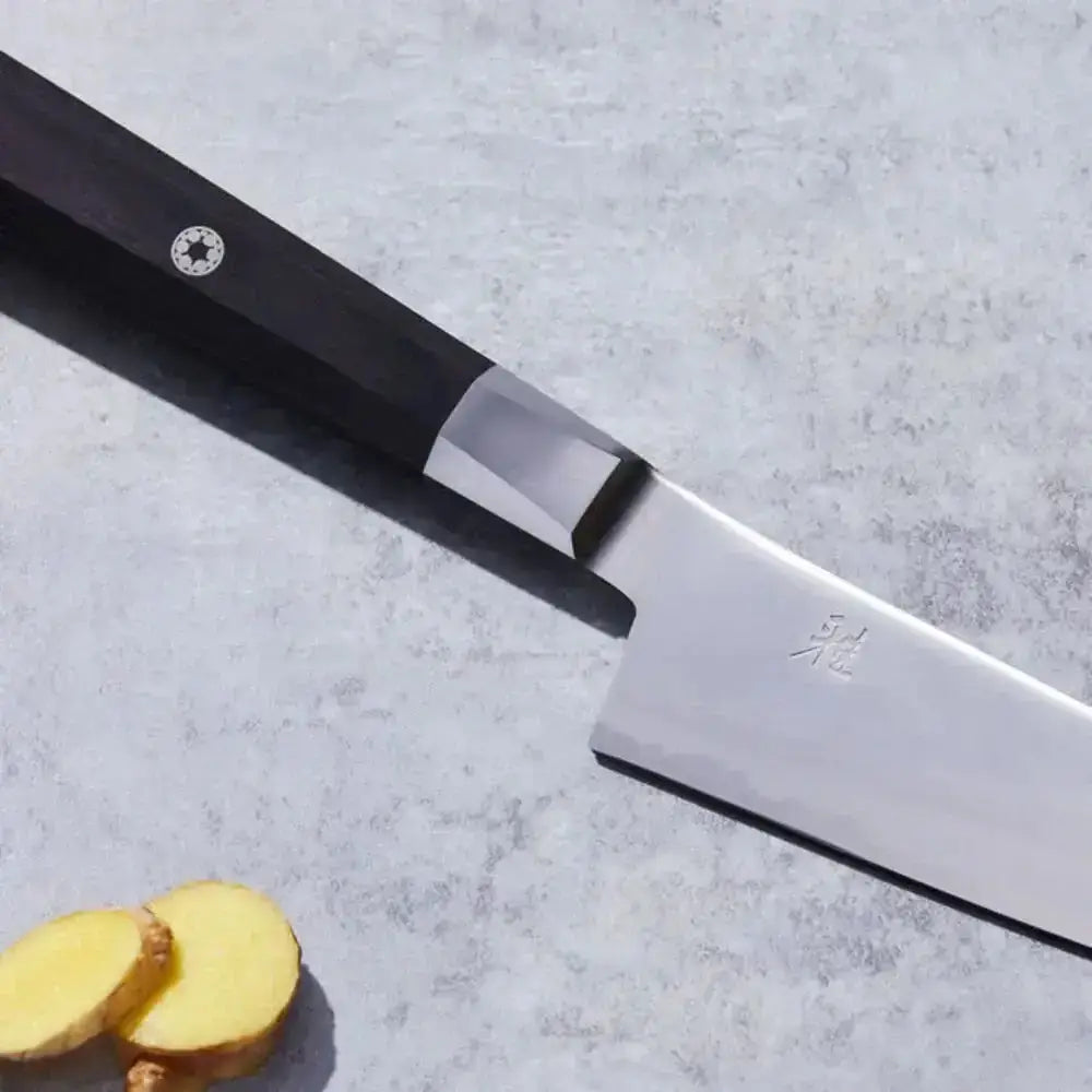 Knife with a black handle and silver blade on a gray surface next to sliced ginger.