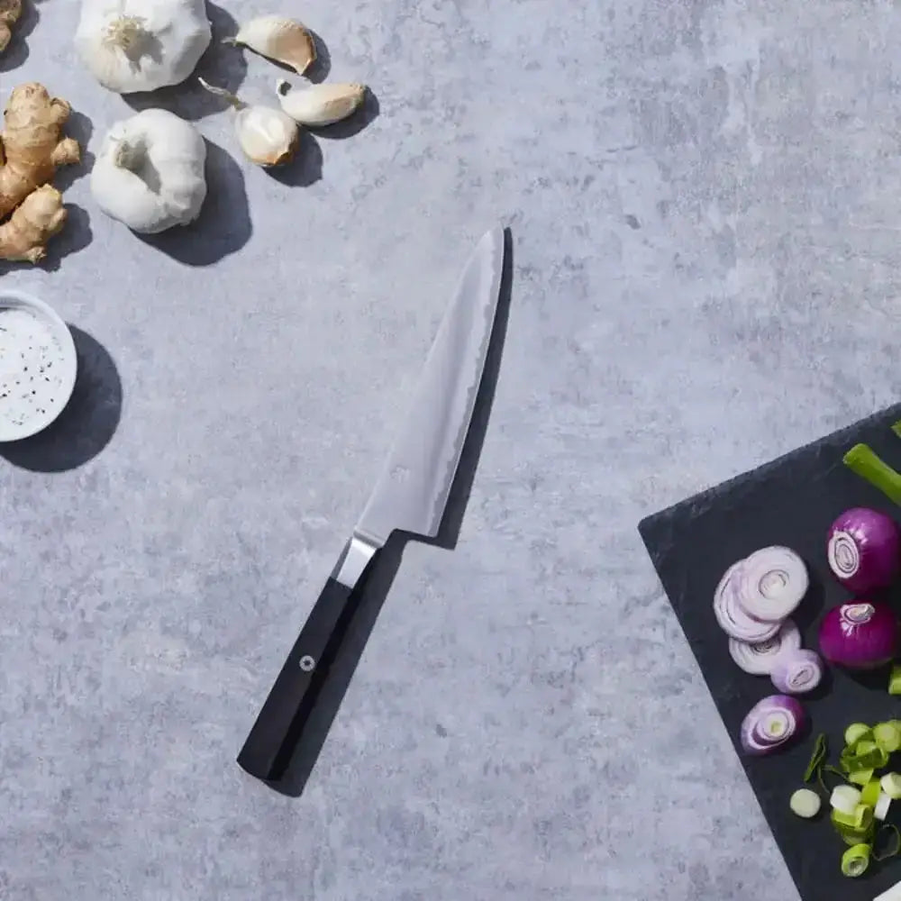 Chef's knife on a gray surface with vegetables around