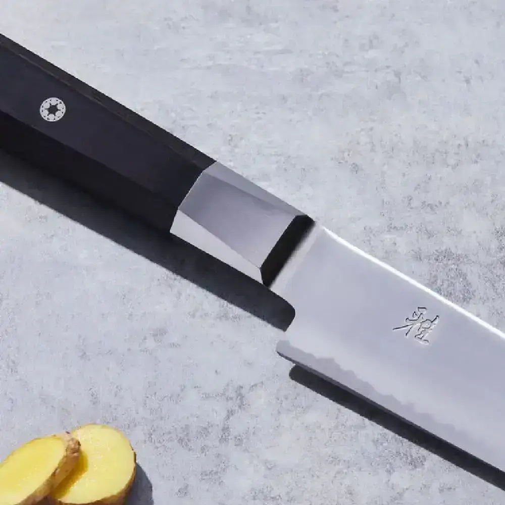 Knife with a black handle and silver blade on a light gray surface, next to a sliced ginger root.