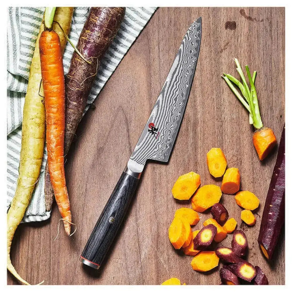  Damascus knife on a wooden cutting board with sliced carrots and whole carrots.