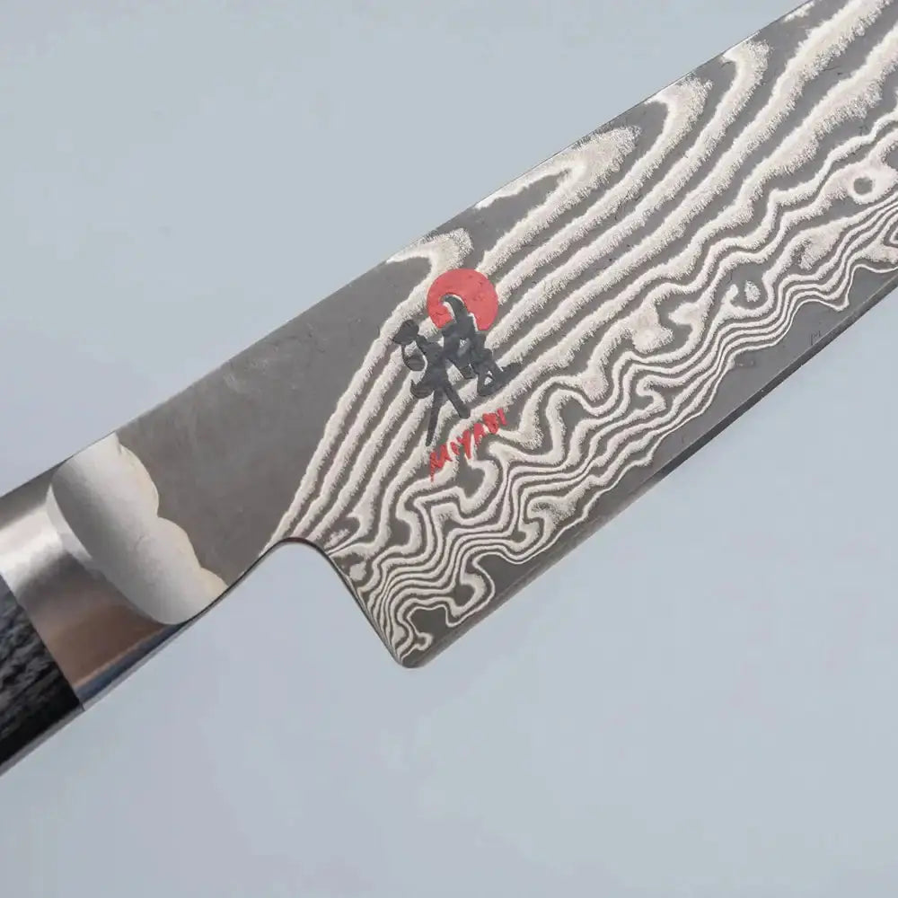 Close-up of a Damascus steel knife blade with a brand logo on a light gray background