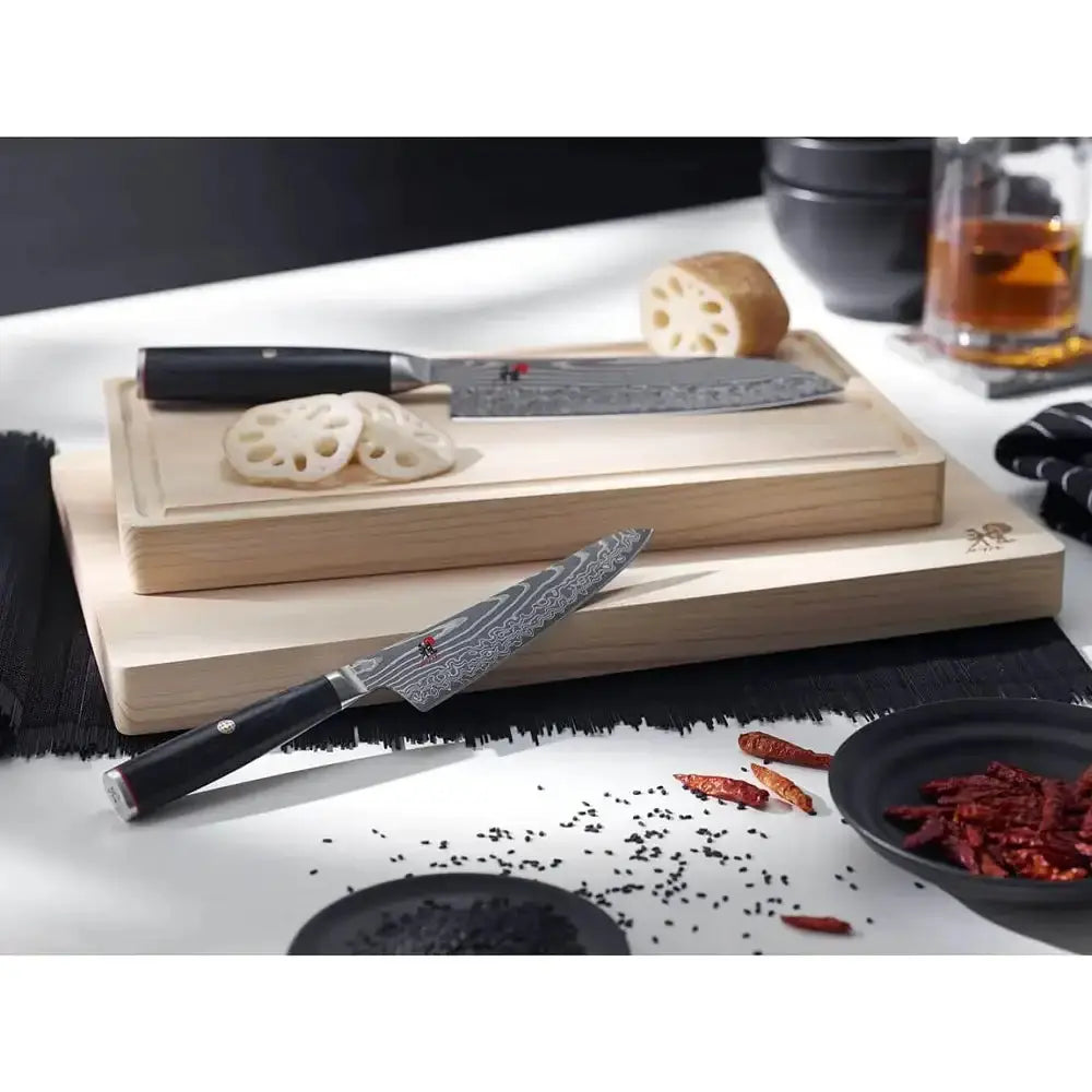 Wooden cutting board with knives and lotus root on a white surface