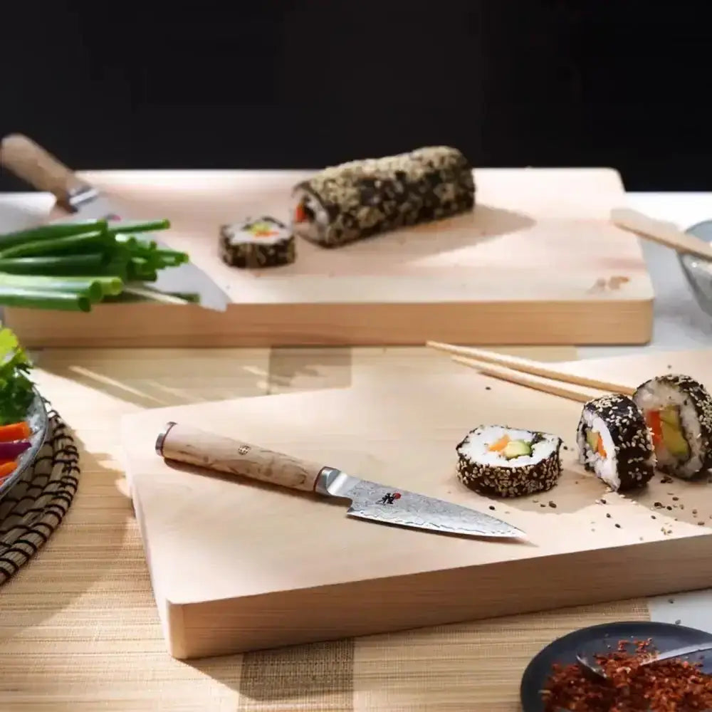 Sushi set with wooden board, knife, and chopsticks on a table.