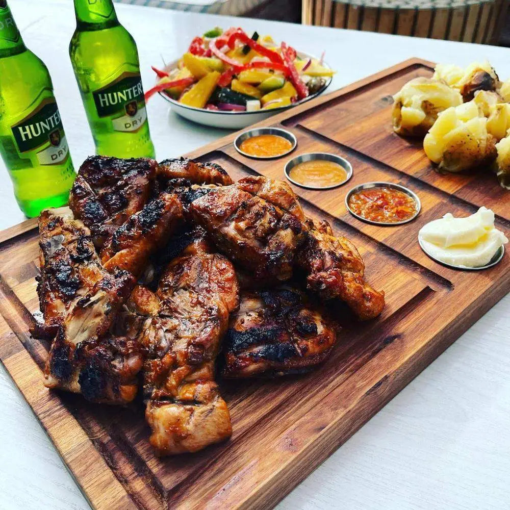 Wooden platter with grilled chicken, sides, and Hunter beer bottles on a table.