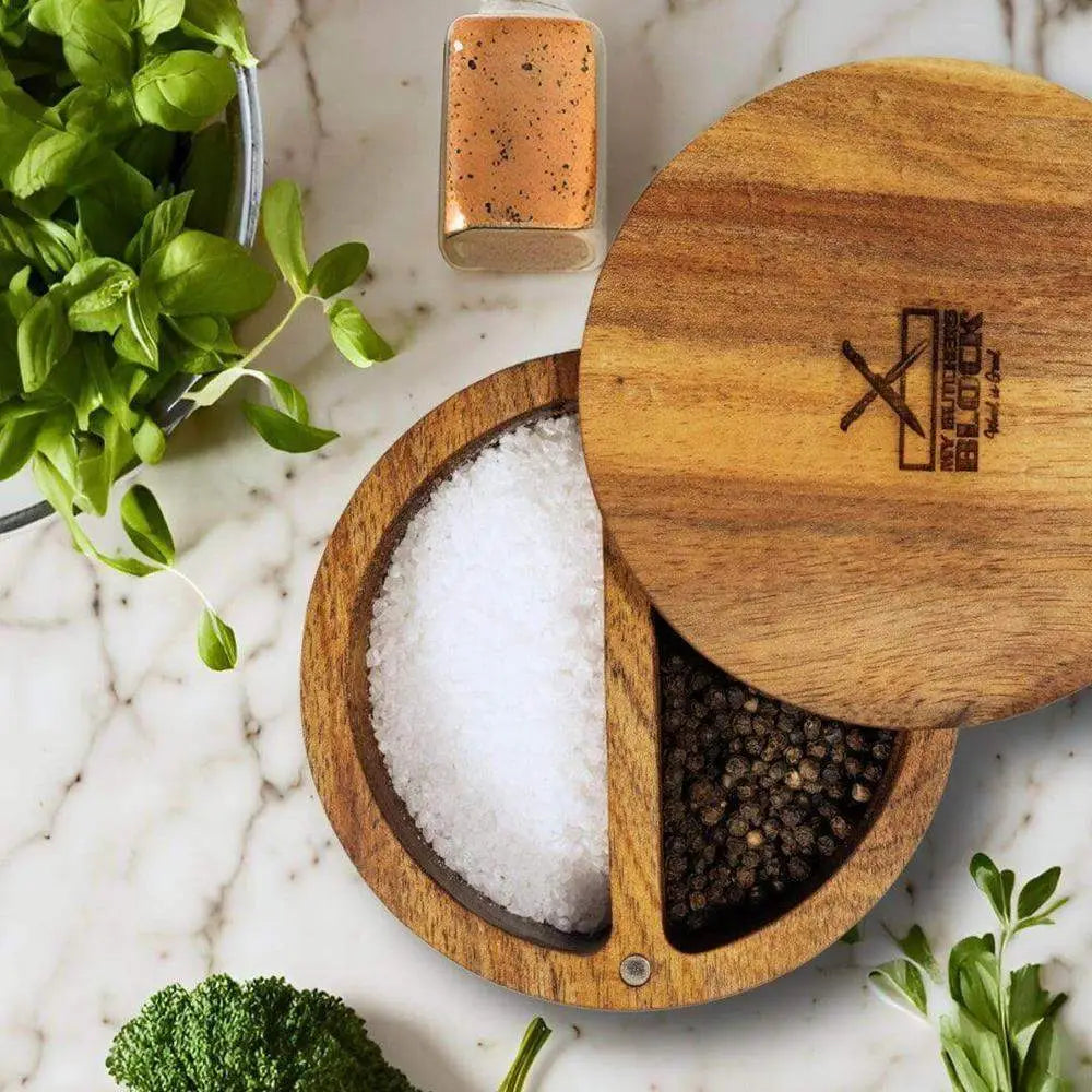 Wooden salt and pepper shaker set on a marble surface with herbs.