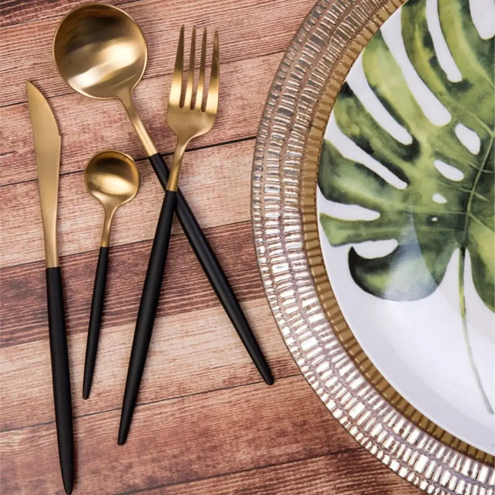 Gold and black cutlery set on a wooden surface with a decorative plate featuring green leaves.