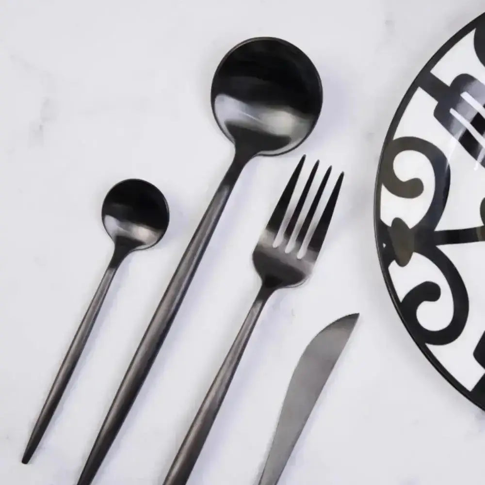 Black cutlery set on a white surface with a decorative plate.