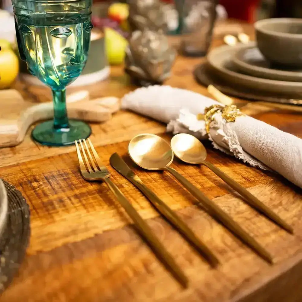 Set of gold cutlery on a wooden table with a blue glass and decorative elements.