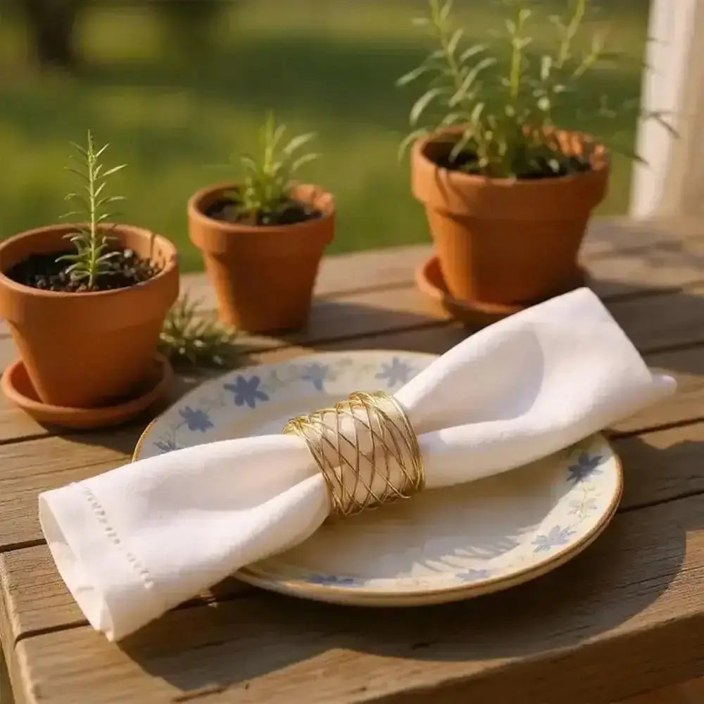 Napkin with a gold napkin ring on a plate, surrounded by potted plants on a wooden table.