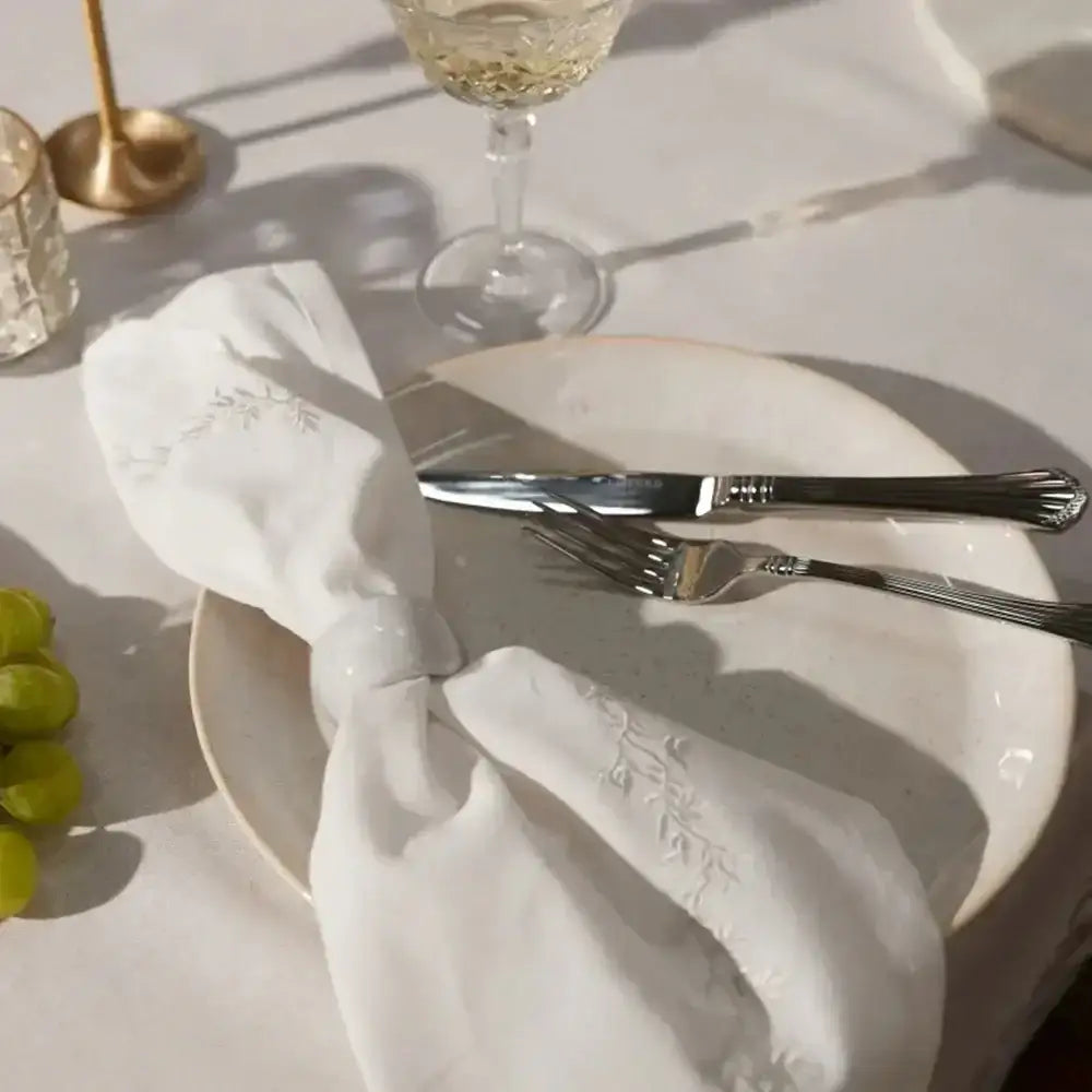 Elegant table setting with white napkin, silverware, and wine glasses on a light surface.