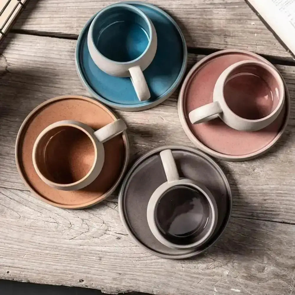 Set of ceramic mugs and saucers in various colors on a wooden surface