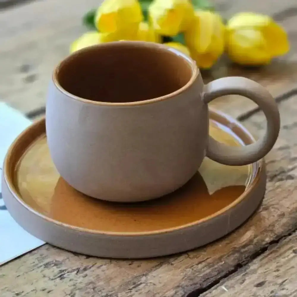 Ceramic cup and saucer on a wooden surface with yellow flowers in the background