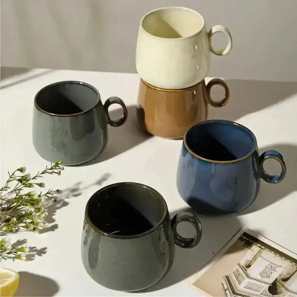 Set of four ceramic mugs in different colors on a light surface with shadows.