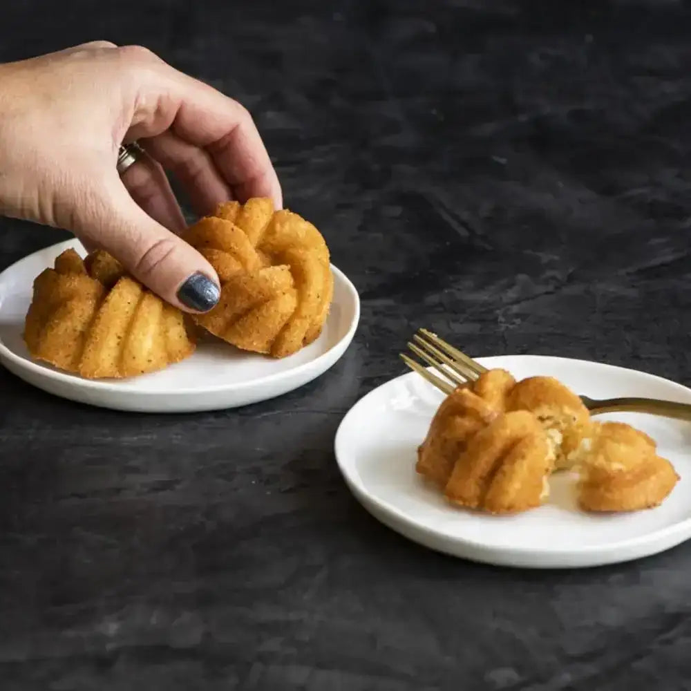 Hand picking up golden braided mini bundt cake on white plate, premium bakeware Cookin Stores