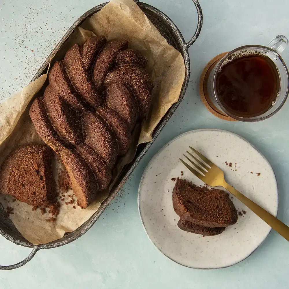 Braided chocolate bundt cake on baking paper with sliced piece on plate and coffee, Cookin Stores kitchenware