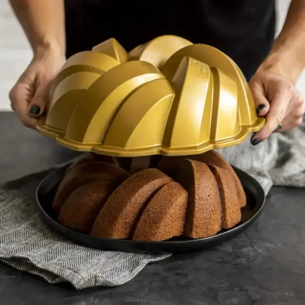 Gold bundt cake mold being removed from a baked cake on a dark surface.