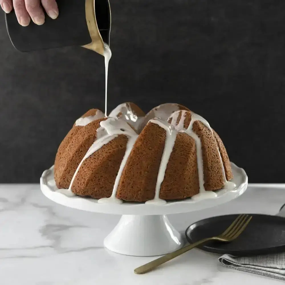 Bundt cake being drizzled with icing on a marble surface with a dark background