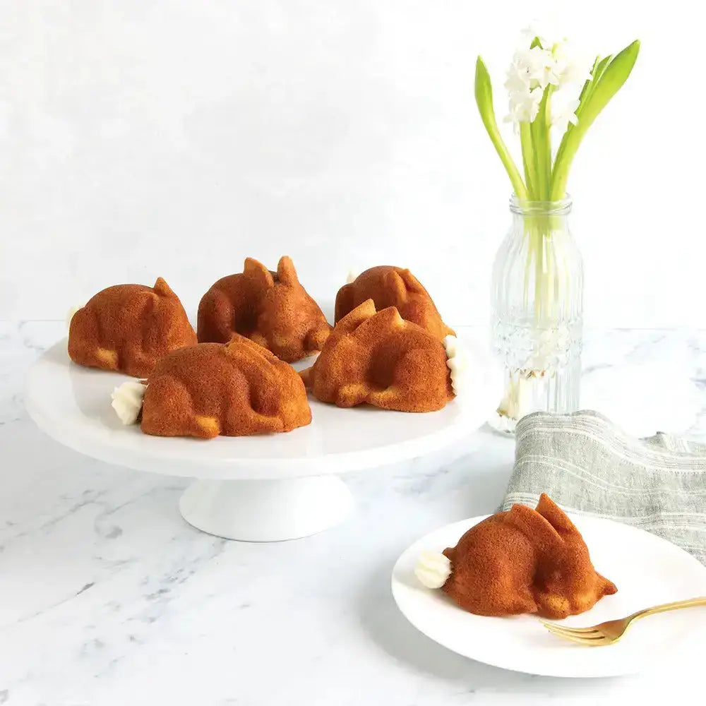 Small bundt cakes shaped like dogs on a white plate with a vase of flowers in the background.