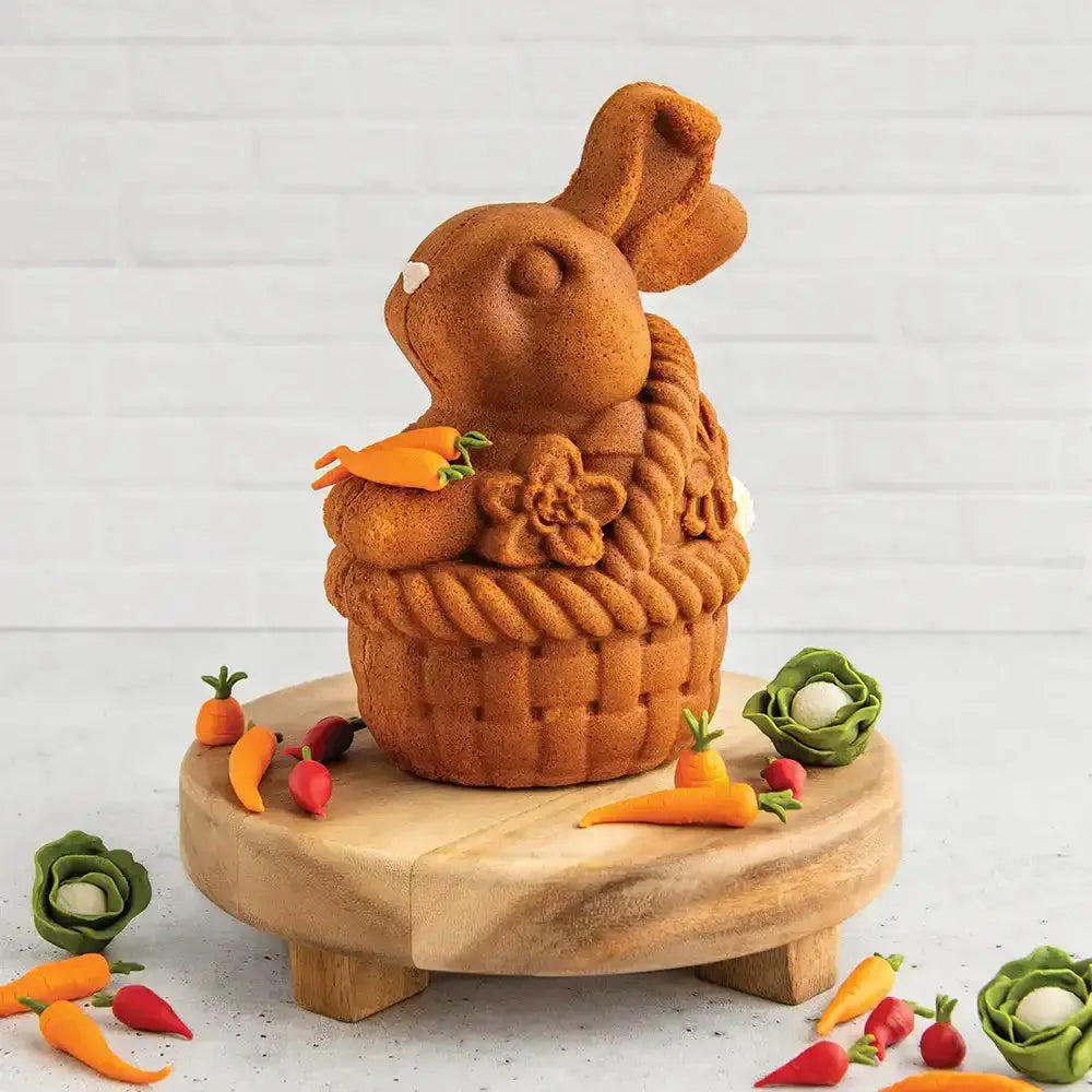 Bunny-shaped cake on a wooden stand with decorative vegetables on a light background