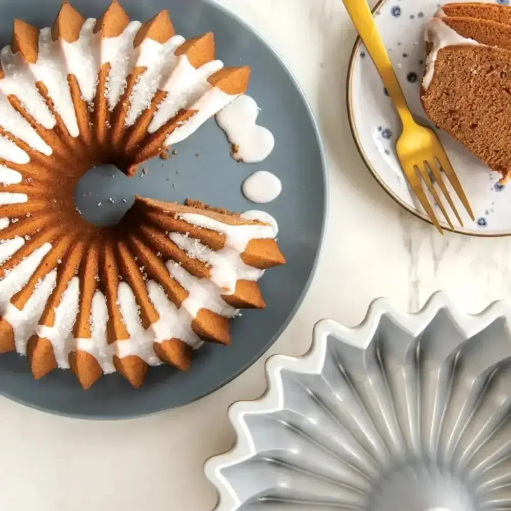 Bundt cake with white frosting on a blue plate, with a metal bundt pan below.