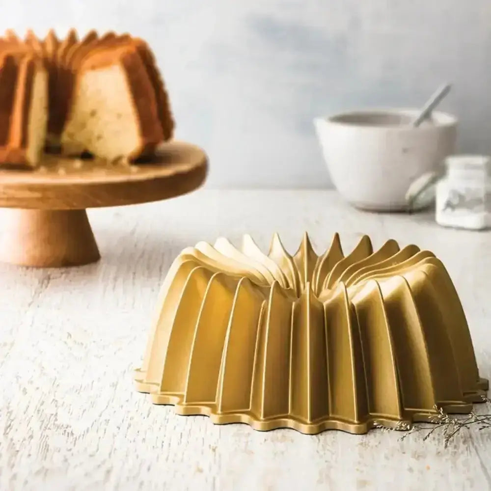 Gold Bundt cake mold on a wooden surface with a cake and kitchen items in the background.