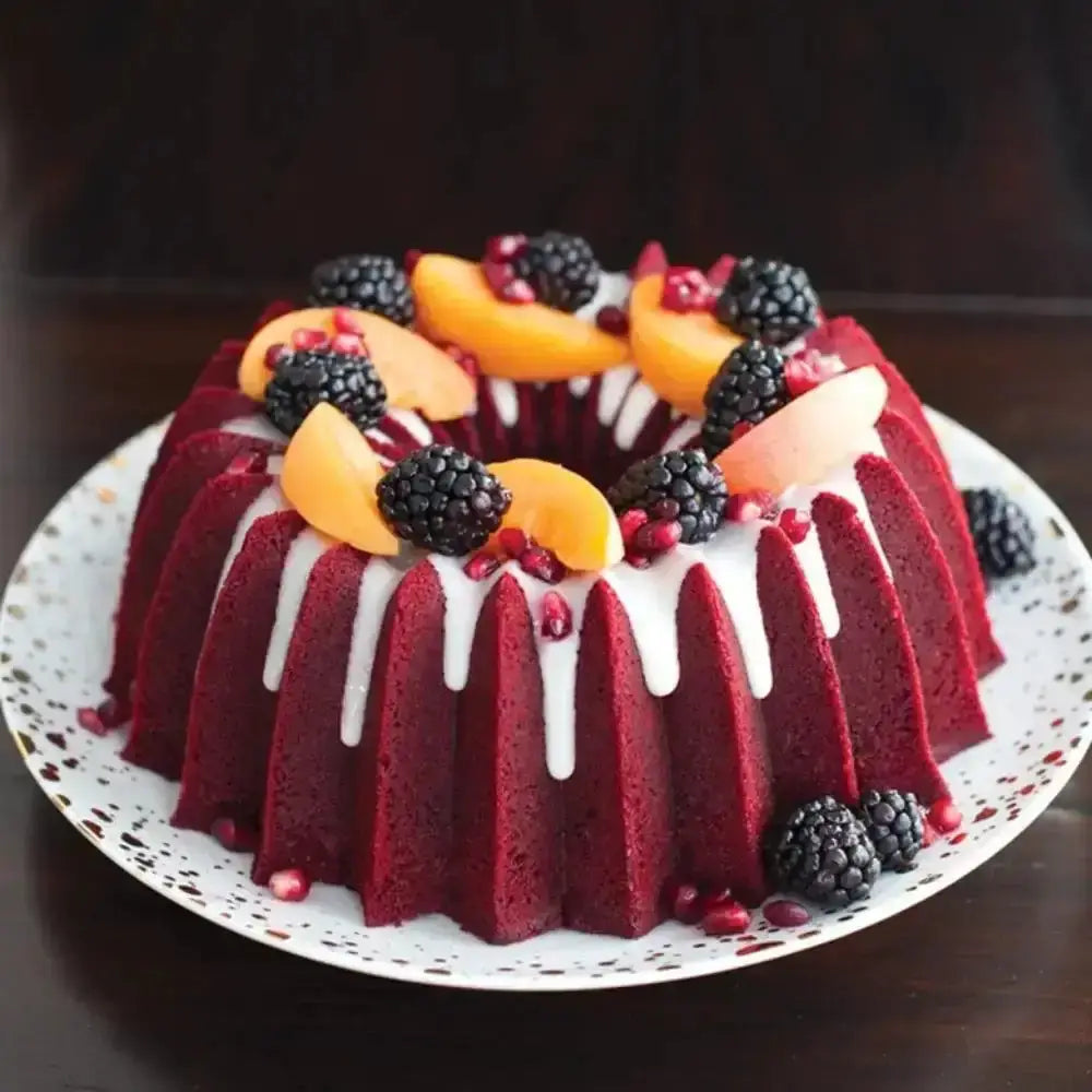 Red velvet bundt cake with white icing, blackberries, and apricots on a white plate.