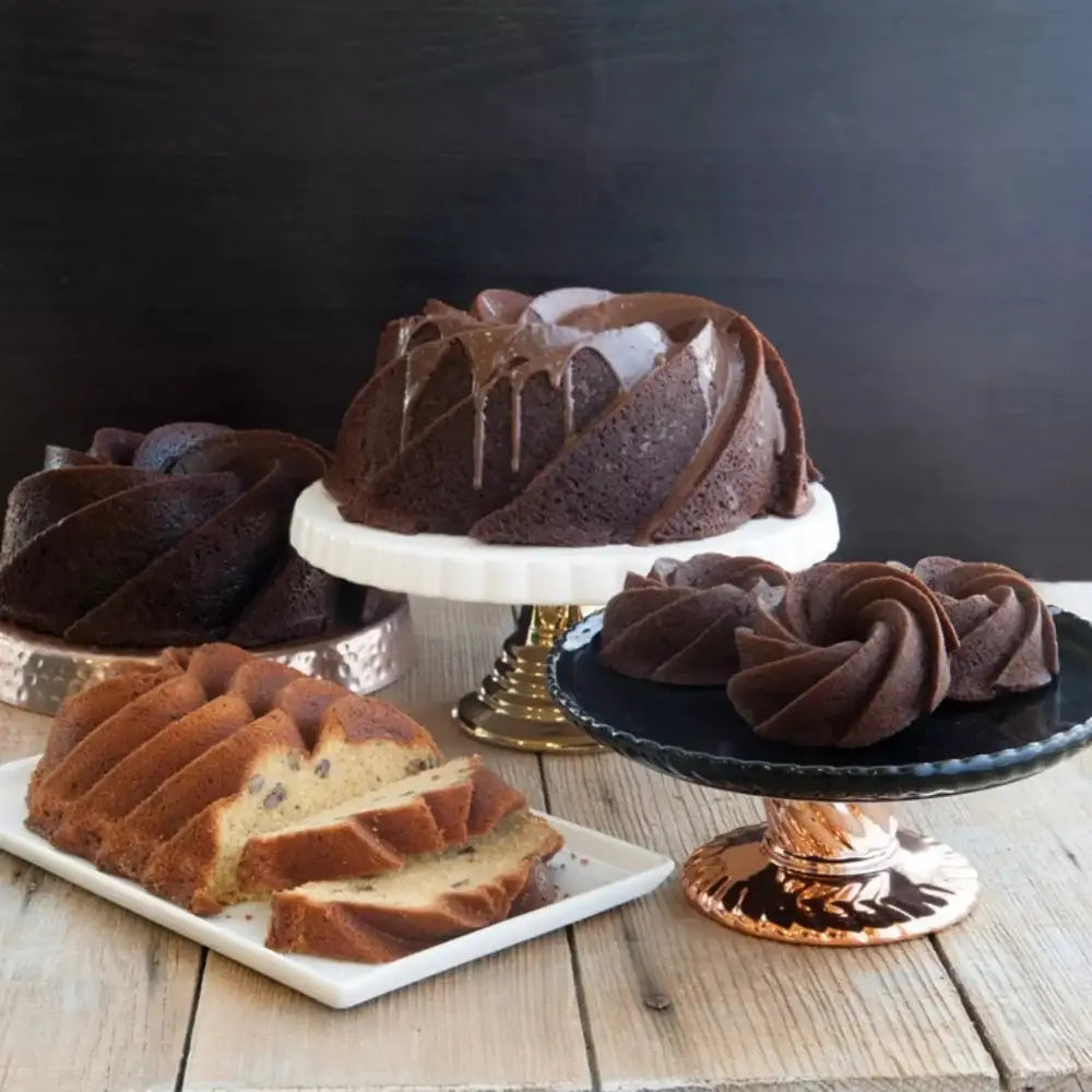 Chocolate bundt cake with glossy glaze on nordic ware gold heritage bundt pan cast aluminum white pedestal stand