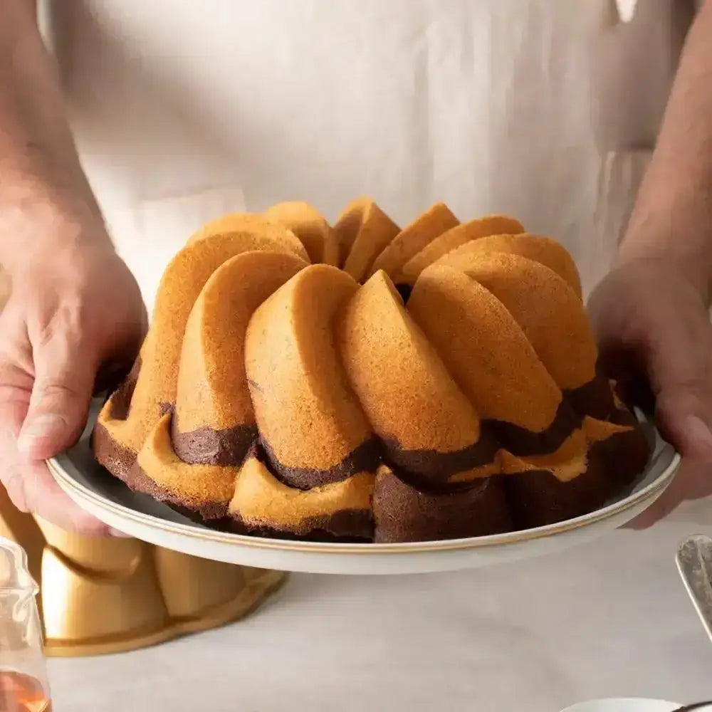 Bundt cake with chocolate swirls on a white plate held by a person.