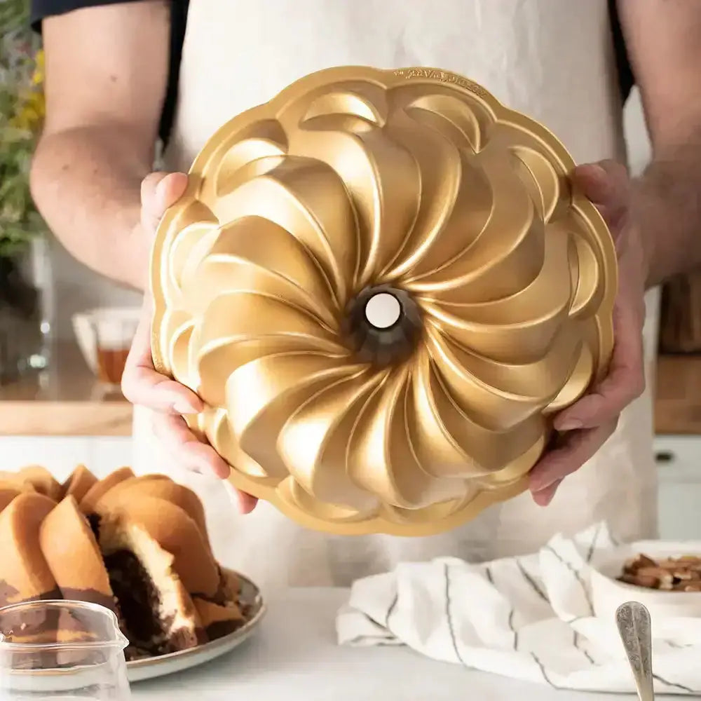 Person holding a gold Bundt cake pan with a baked cake in the background