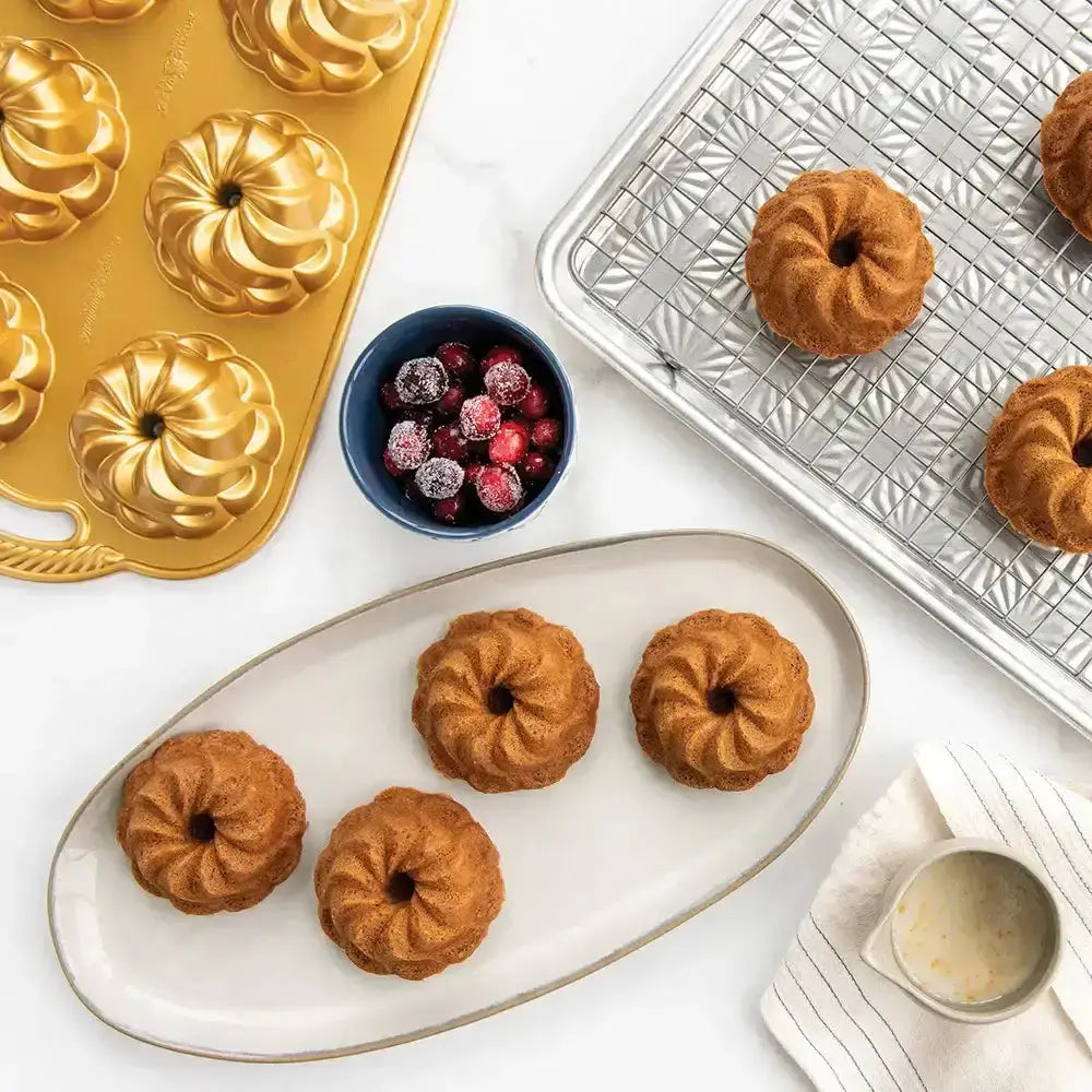 Baked donuts on a tray with a baking pan, gold donut mold, and bowl of berries.