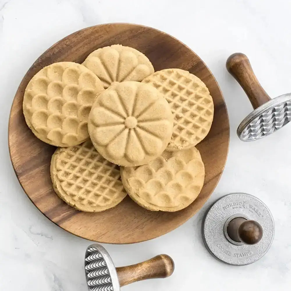 Wooden plate with waffle cookies and cookie cutters on a white background