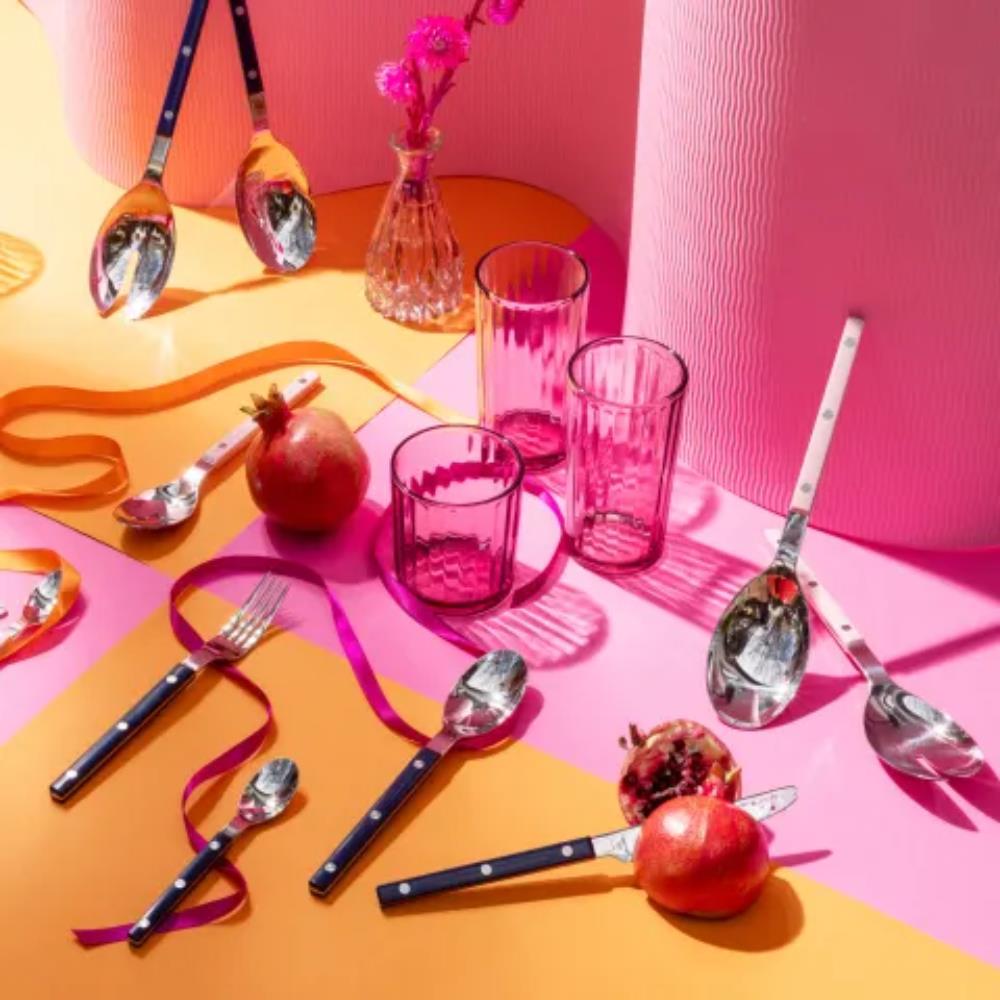 Colorful table setting with pink glasses, spoons, forks, and pomegranates on a pink and orange background.