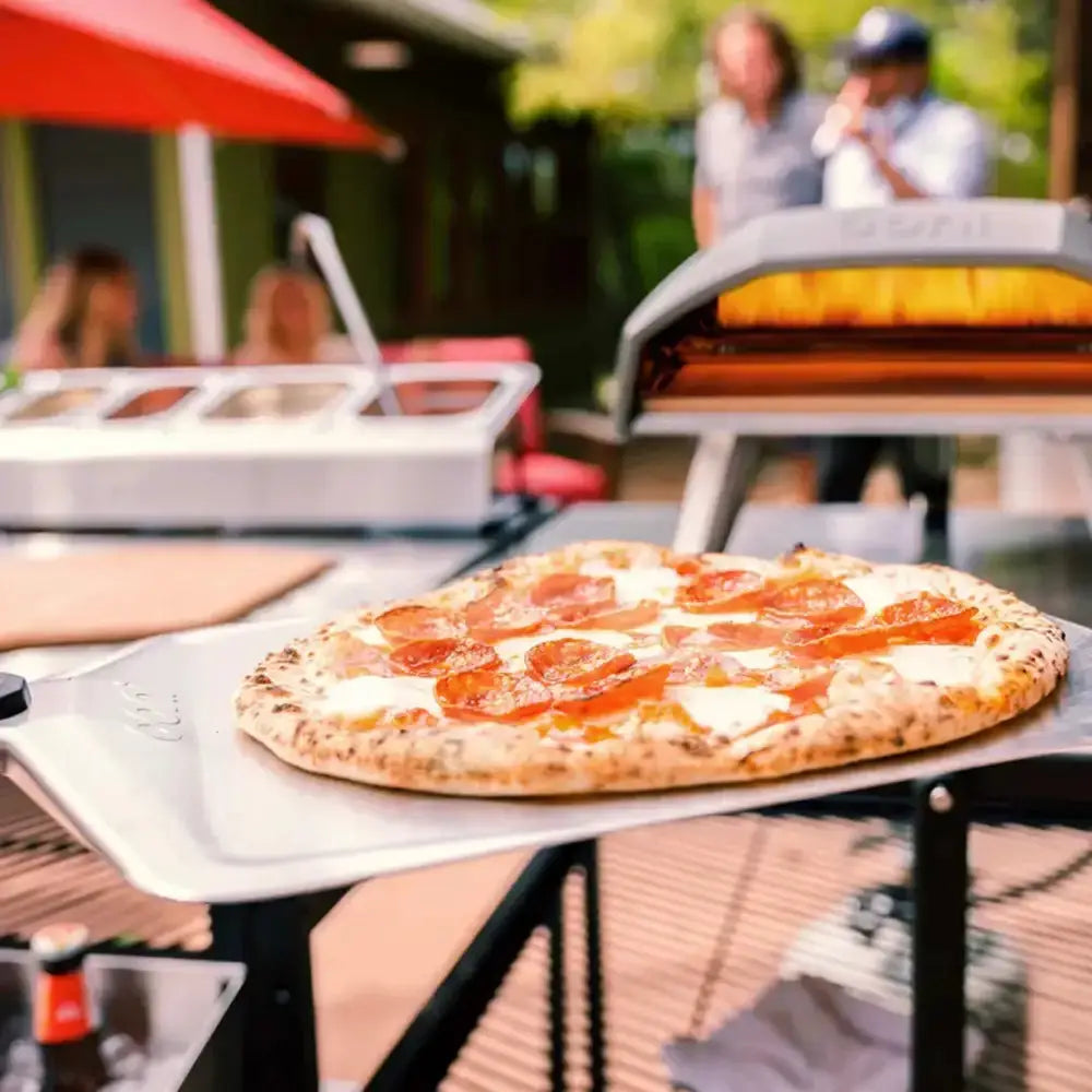 Pepperoni pizza on a table with outdoor setting and people in the background