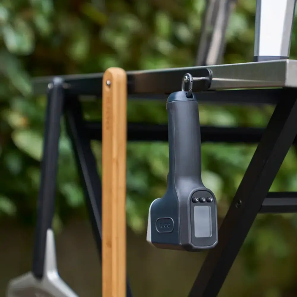 Digital weight scale hanging on a metal bar with a blurred green background