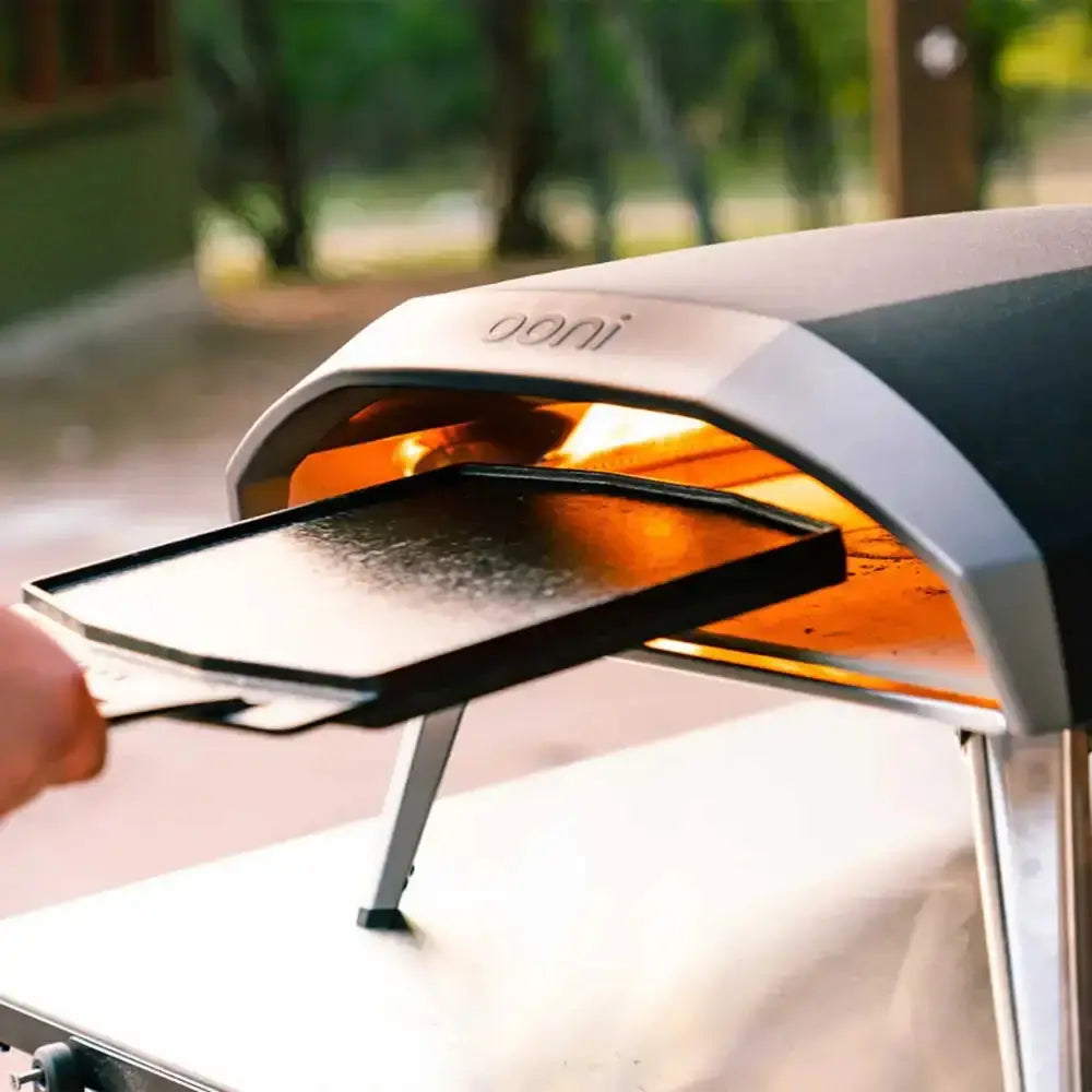 Silver and black ooni pizza oven with glowing interior and rectangular cast iron grizzler plate being pulled out