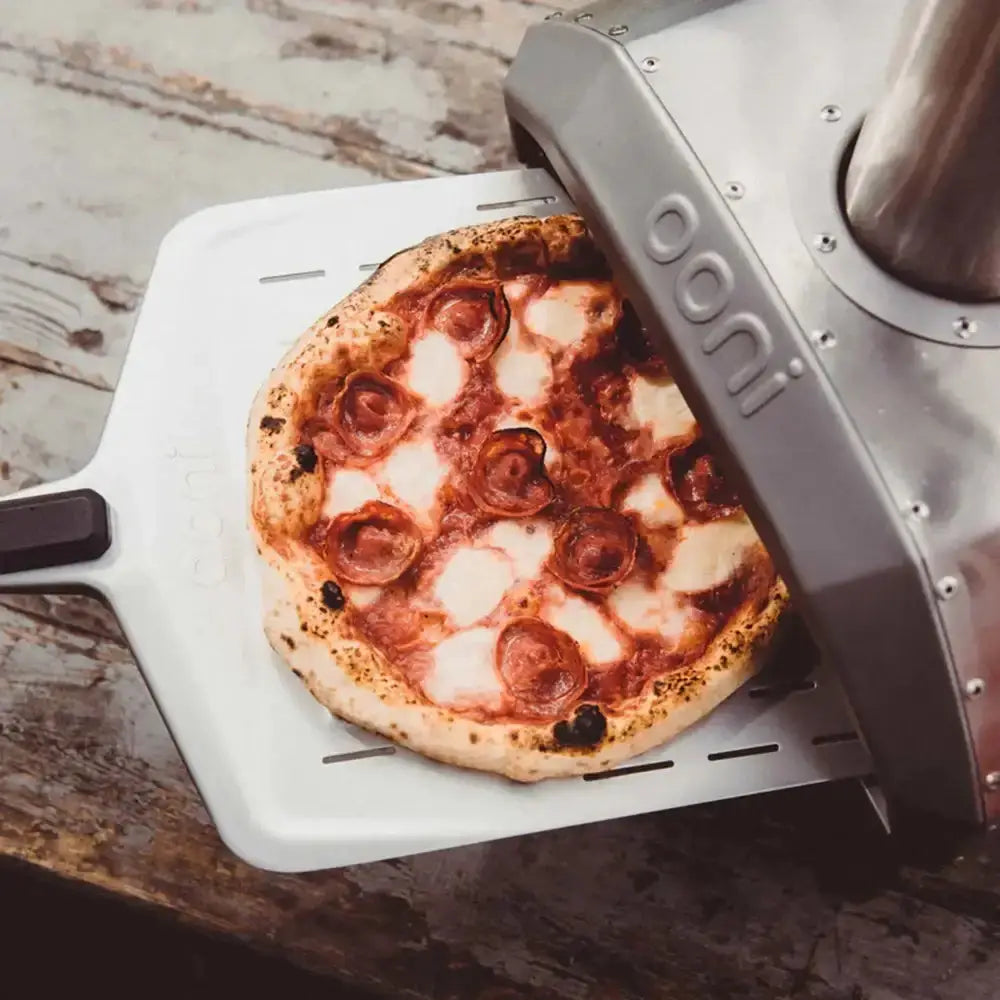 Pizza being taken out of a portable pizza oven with 'Don"i' branding.