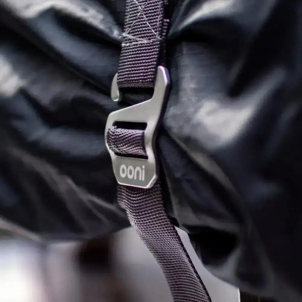 Silver-toned metal buckle with ooni branding securing a dark gray woven strap on black ooni karu pizza oven cover