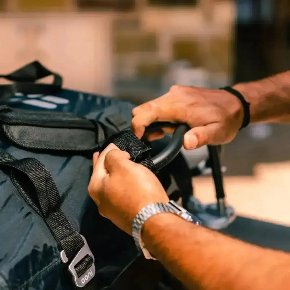 Person securing a black strap on a blue bag with a blurred background